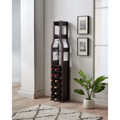 a tall wooden wine rack with bottles in it next to a potted plant and pictures on the wall