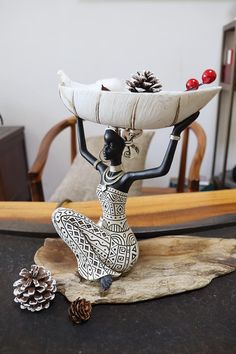 a figurine sitting on top of a table holding a tray with pine cones