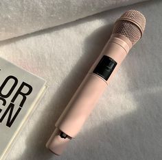 a pink microphone sitting on top of a white sheet next to a book and pen