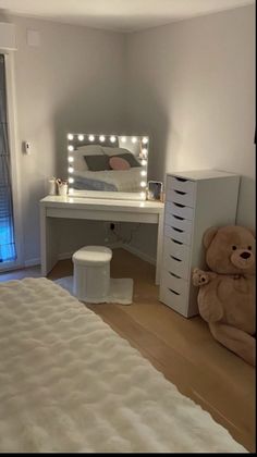 a teddy bear sitting in front of a desk with a mirror and lights on it