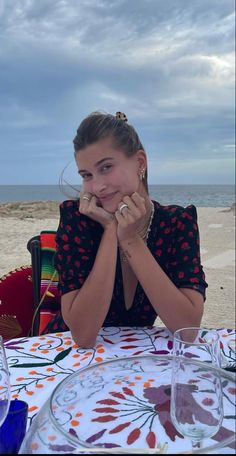 a woman sitting at a table in front of the ocean with her hands on her face