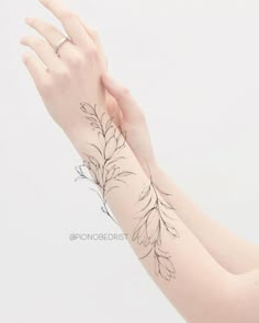 a woman's arm with a tattoo on it that has flowers and leaves drawn on it