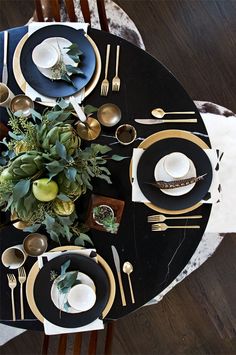 the table is set with black and gold plates, silverware, and green plants