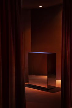 an empty room with red curtains and a mirrored cube in the center, lit by a spot light