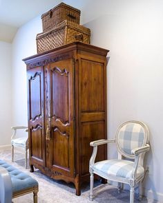 an armoire in the corner of a room with a chair and basket on top