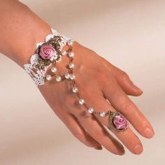 a woman's hand with pink roses and pearls on the ring finger, wearing a lace bracelet