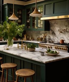 a kitchen with green cabinets and marble counter tops, gold pendant lights over the island