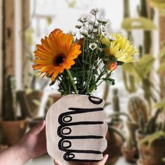 a hand holding a vase with flowers in it and the word mom written on it