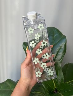 a hand holding a bottle filled with flowers on top of a green leafy plant