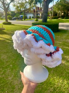 a hand holding up a knitted hat on top of a white mannequin head