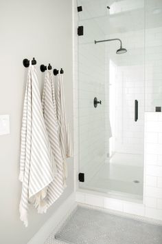 two towels hanging on the wall in front of a shower with white tiles and black handles