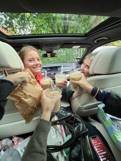 two women sitting in the back seat of a car drinking coffee and talking to each other