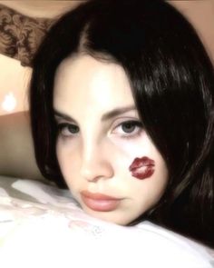 a woman laying on top of a bed with her eyes closed and lipstick painted on her face