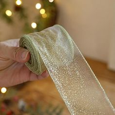 a hand is holding a roll of glittered ribbon in front of a christmas tree