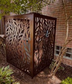 a metal box sitting in the middle of a garden next to a brick wall and trees