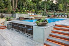 an outdoor bar with stools next to a swimming pool in the middle of a wooded area