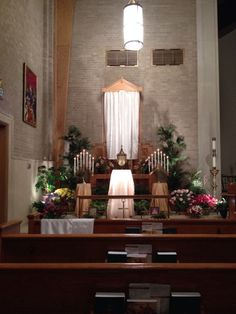 the interior of a church with wooden pews and flowers on the alter, decorated with greenery