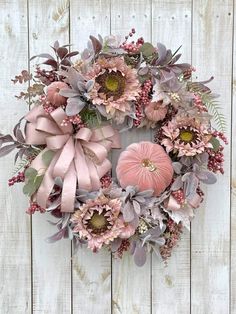 a wreath with pink flowers and green leaves on a white wooden background is hanging on the wall