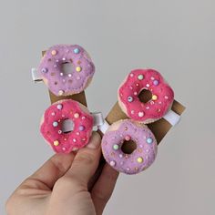 a hand holding three doughnuts with sprinkles on them