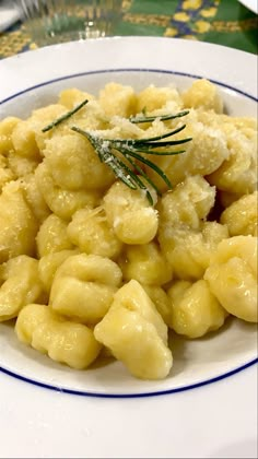 a white plate topped with macaroni and cheese covered in gravy, garnished with a sprig of rosemary