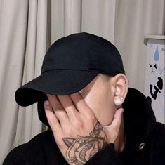 a man wearing a black hat covering his face with his hands and holding his nose