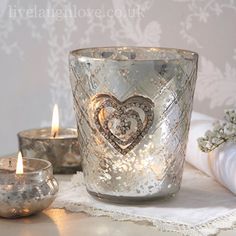 two candles are sitting next to each other on a white tablecloth with silver hearts