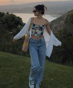 a woman walking on top of a lush green hillside next to the ocean at sunset