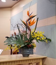 an arrangement of tropical flowers in a vase on a wooden table next to a wall