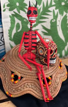 a red and black skeleton sitting on top of a wooden table next to a pillow