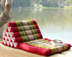 a red and green patchwork chaise lounge chair next to a lake