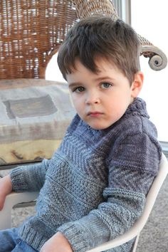 a little boy sitting in a chair with a hat on his head and looking at the camera