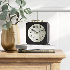 a clock sitting on top of a wooden table next to a vase filled with flowers