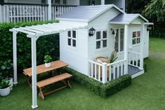 a small white house sitting on top of a lush green field next to a wooden bench