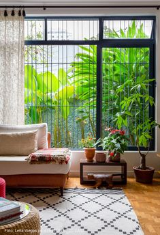 a living room filled with furniture next to a window covered in green plants and potted plants