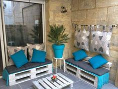 a patio with blue cushions and wooden pallets on the floor, next to a potted plant