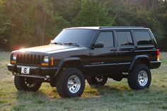 a black jeep parked on top of a grass covered field in front of some trees