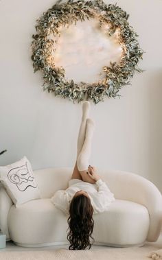 a woman laying on top of a white couch in front of a wreath hanging above her head