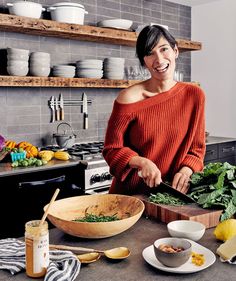 a woman in an orange sweater chopping vegetables on a kitchen counter with plates and bowls