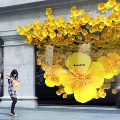 a woman standing in front of a store window with yellow flowers on the windowsill