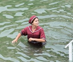 a woman in the water wearing a red shirt and a hat is sitting on a boat