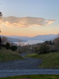 the sun is setting over some hills and water in the distance, with sheep grazing on the grass