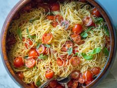 a bowl filled with pasta and tomatoes on top of a table next to a spoon