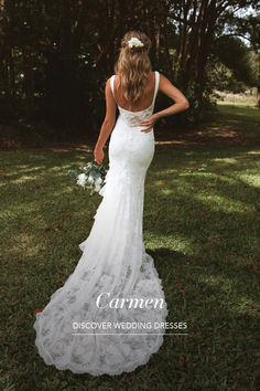 the back of a woman in a wedding dress standing on grass with trees behind her