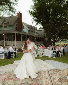 a bride and groom dance on the ground at their wedding reception in front of a large house