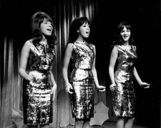 three women in sequin dresses singing on stage