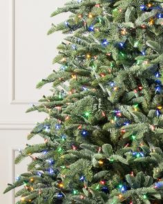 a green christmas tree with multicolored lights in front of a white wall and door