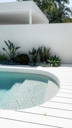 an empty swimming pool in front of a white fence with plants growing on the side