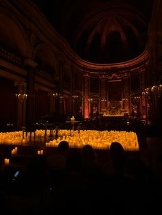 a large room filled with lots of yellow candles in front of a piano and stage