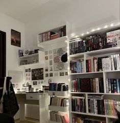 a room filled with lots of books next to a white desk and bookcases