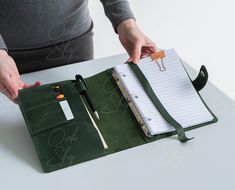 a person is holding a pen and writing on a green binder next to a notebook